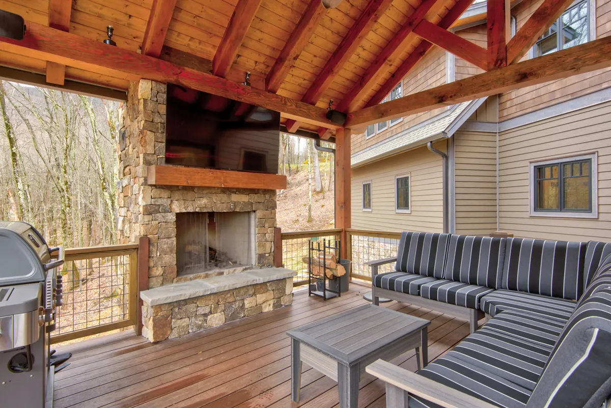 A cozy outdoor living space featuring a stone fireplace, comfortable seating, grill, and wooden beams, creating an ideal spot for gathering, storytelling, or cooking outdoors. The setup invites guests to enjoy sunsets, game nights, or simply unwind by the fire.