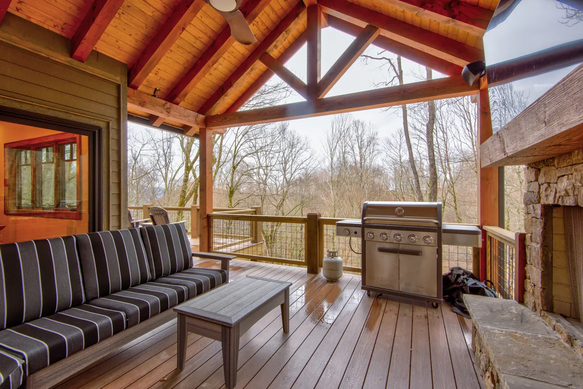 An outdoor seating area with a grill, cozy wooden beams overhead, and tranquil views of the surrounding trees. The space is designed for relaxation, outdoor cooking, and socializing in a natural setting, offering a seamless indoor-outdoor living experience.