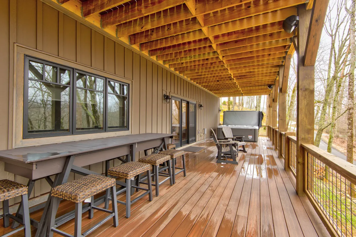 This image focuses on a long bar table with stools on a wooden deck, complemented by a comfortable seating area. The outdoor vibe is casual and inviting, perfect for socializing, outdoor dining, or celebrating special occasions while enjoying scenic views.