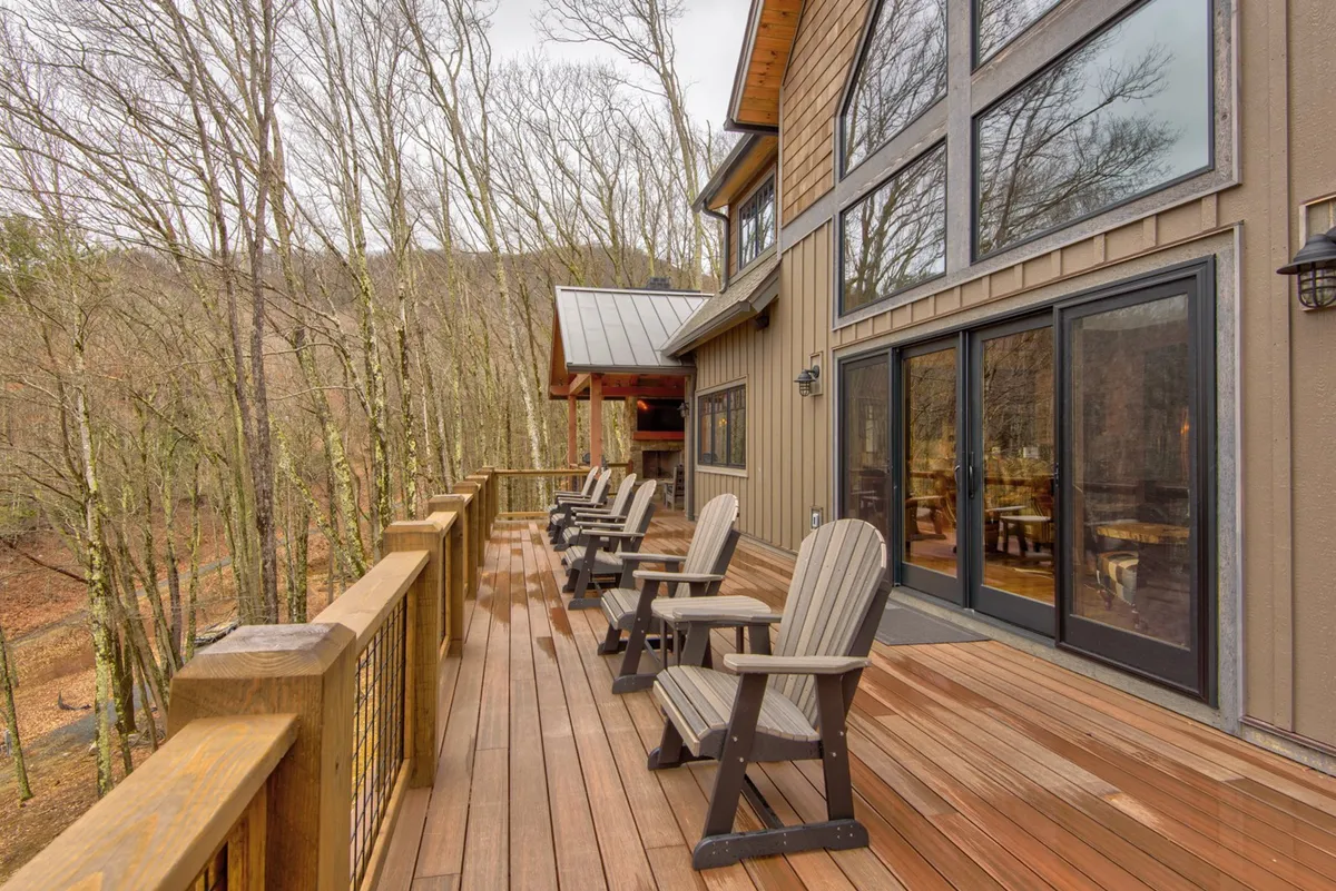 The photo shows a serene wooden deck with comfortable deck chairs, large windows, and a lush backdrop of surrounding trees. The atmosphere is peaceful, ideal for enjoying morning coffee, sunsets, or quiet moments in nature.