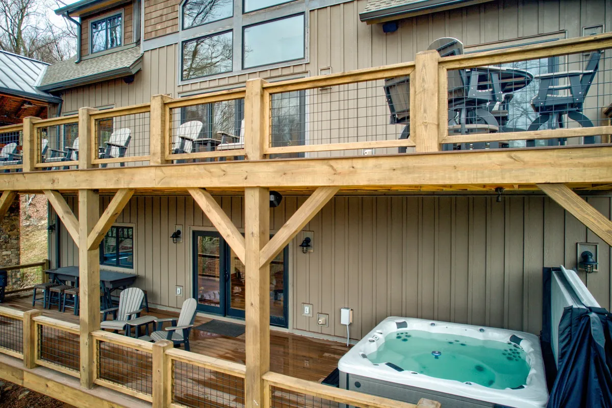 This image captures a wooden deck featuring a private hot tub, outdoor seating, and large windows with views of the surrounding natural landscape. The tranquil mood is enhanced by the seamless connection between indoor comfort and outdoor beauty, inviting guests to unwind and socialize while soaking in mountain views.